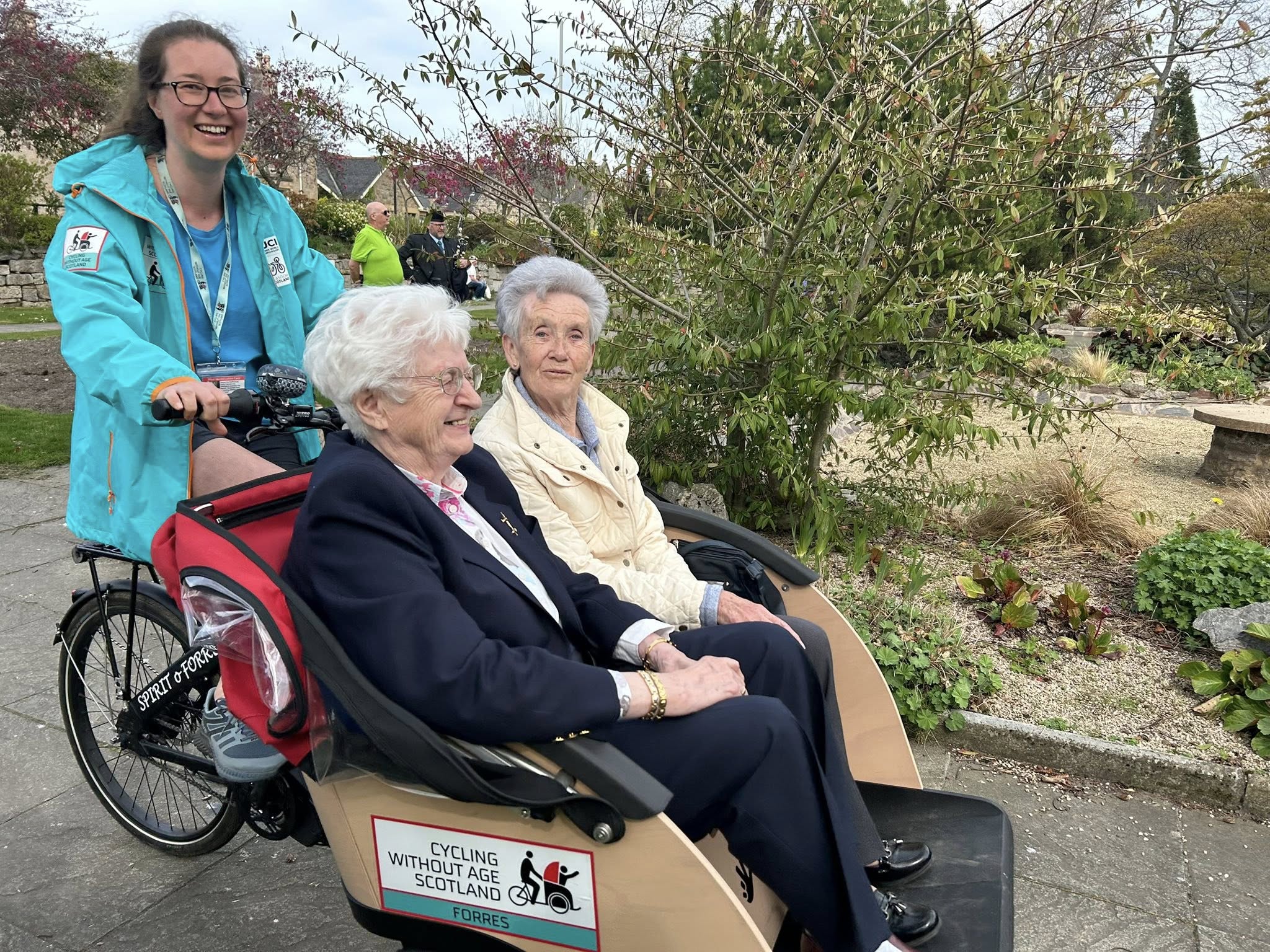 A lady smiles as she pilots a trishaw, which is carrying two ladies around a local park. 
