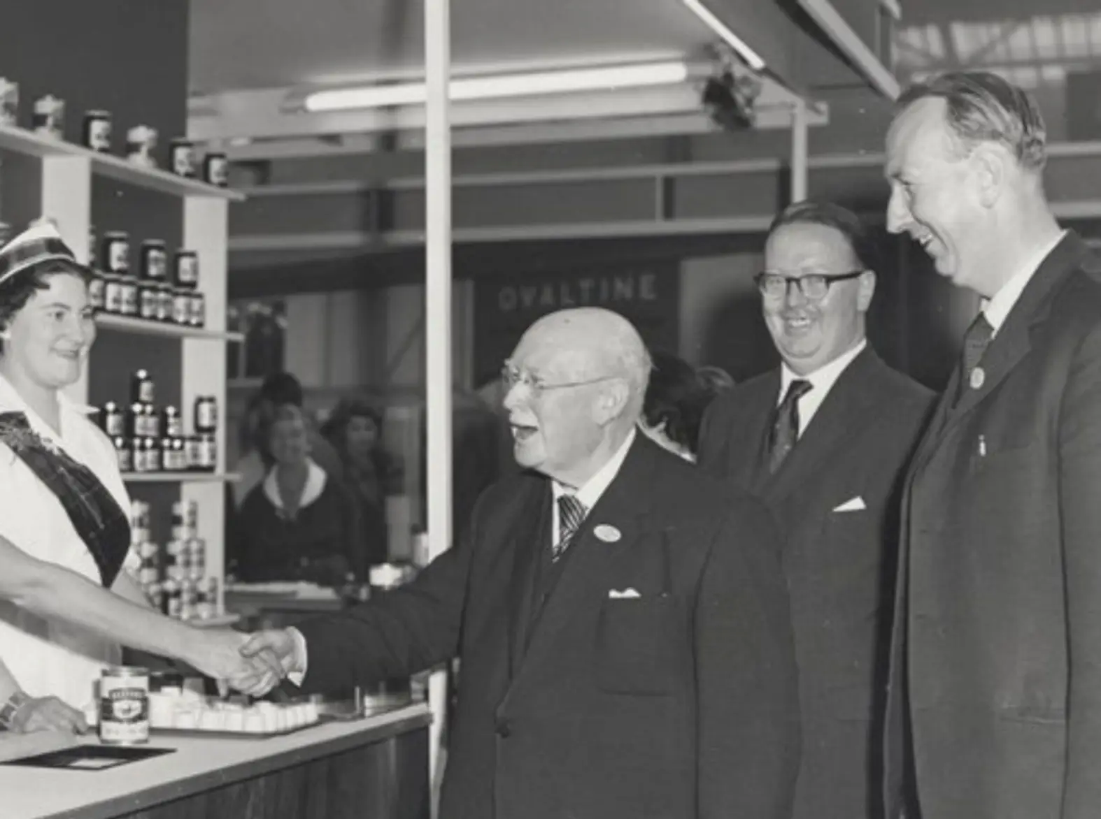 A black and white images shows William Baxter visiting a trade stand, where soups from Baxters of Speyside are being showcased. Behind William are his sons Gordon and Ian.